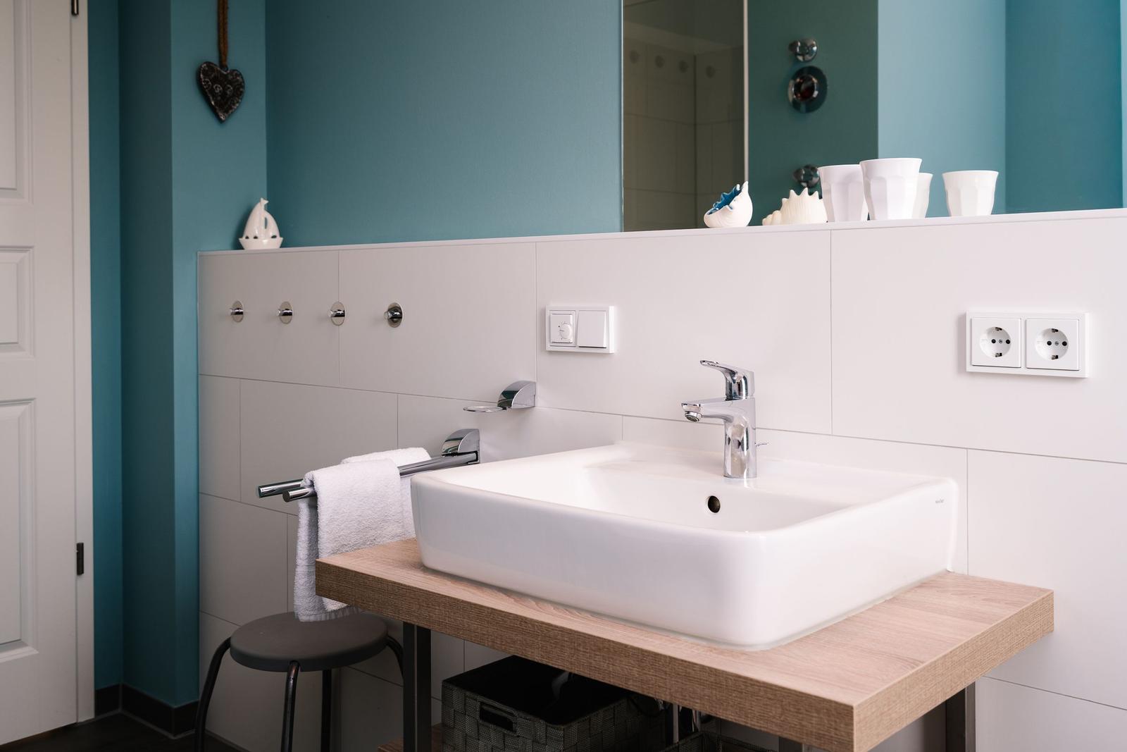 Badezimmer mit Waschbecken auf Holzkonsole, Spiegel und weißen Fliesen.