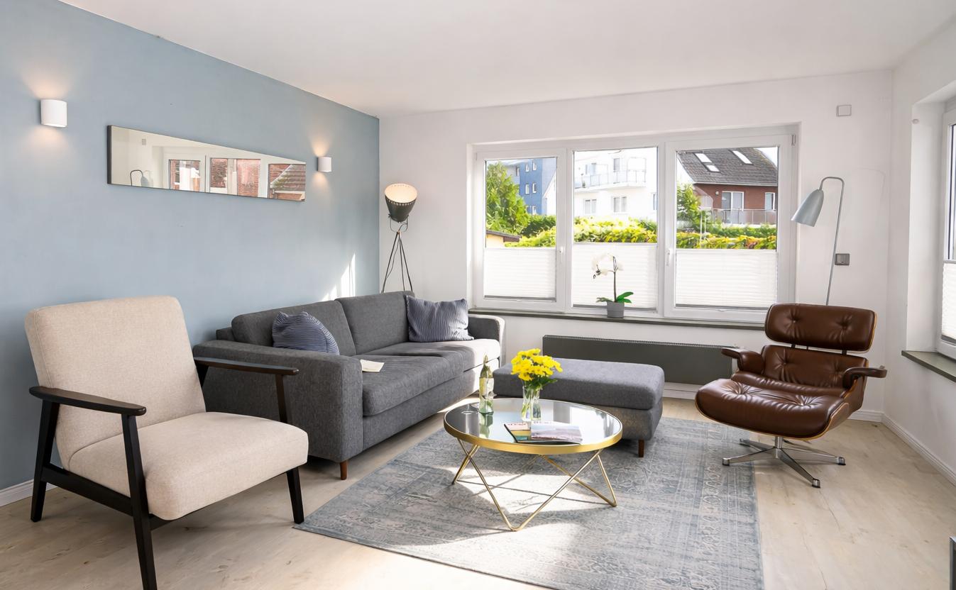 Wohnzimmer mit grauem Sofa, braunem Sessel und Glas-Tisch.