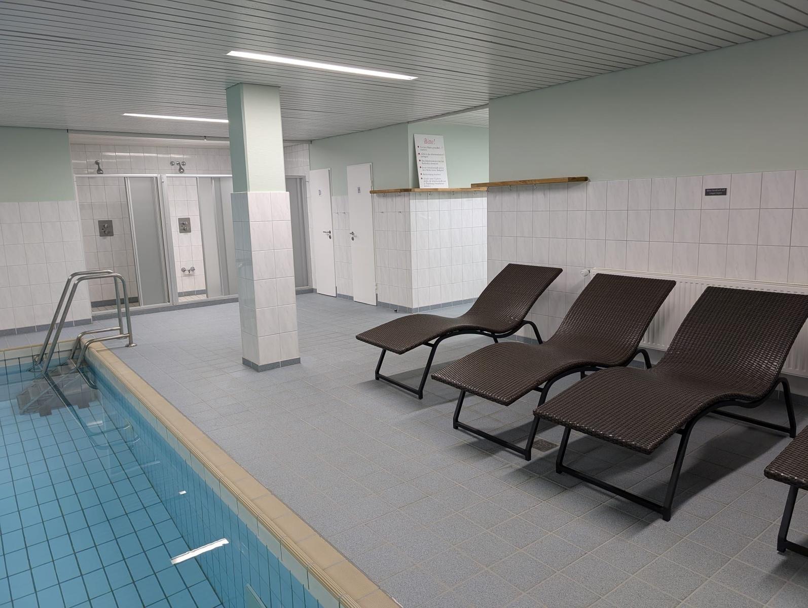 Innenpool mit Liegestühlen und Duschen im Hintergrund.