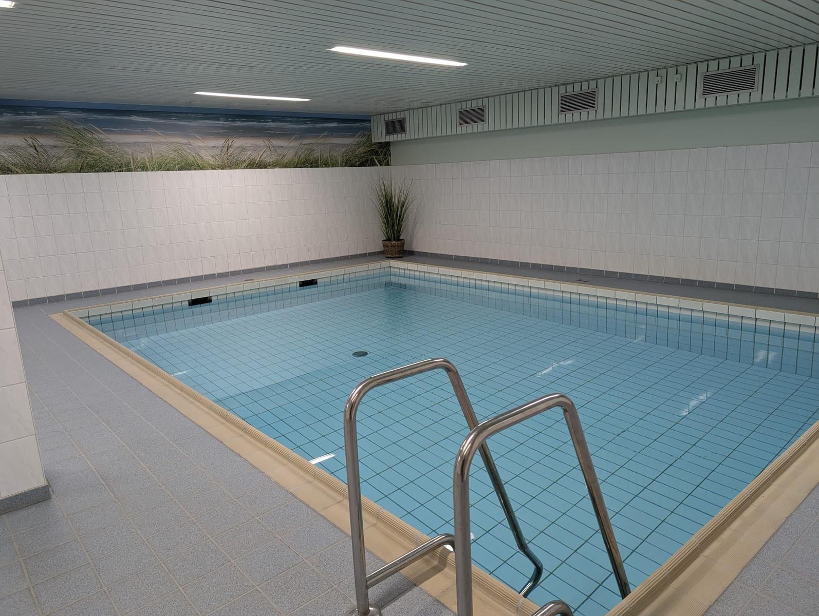 Innere Schwimmhalle mit Pool und Strandbild an der Wand.
