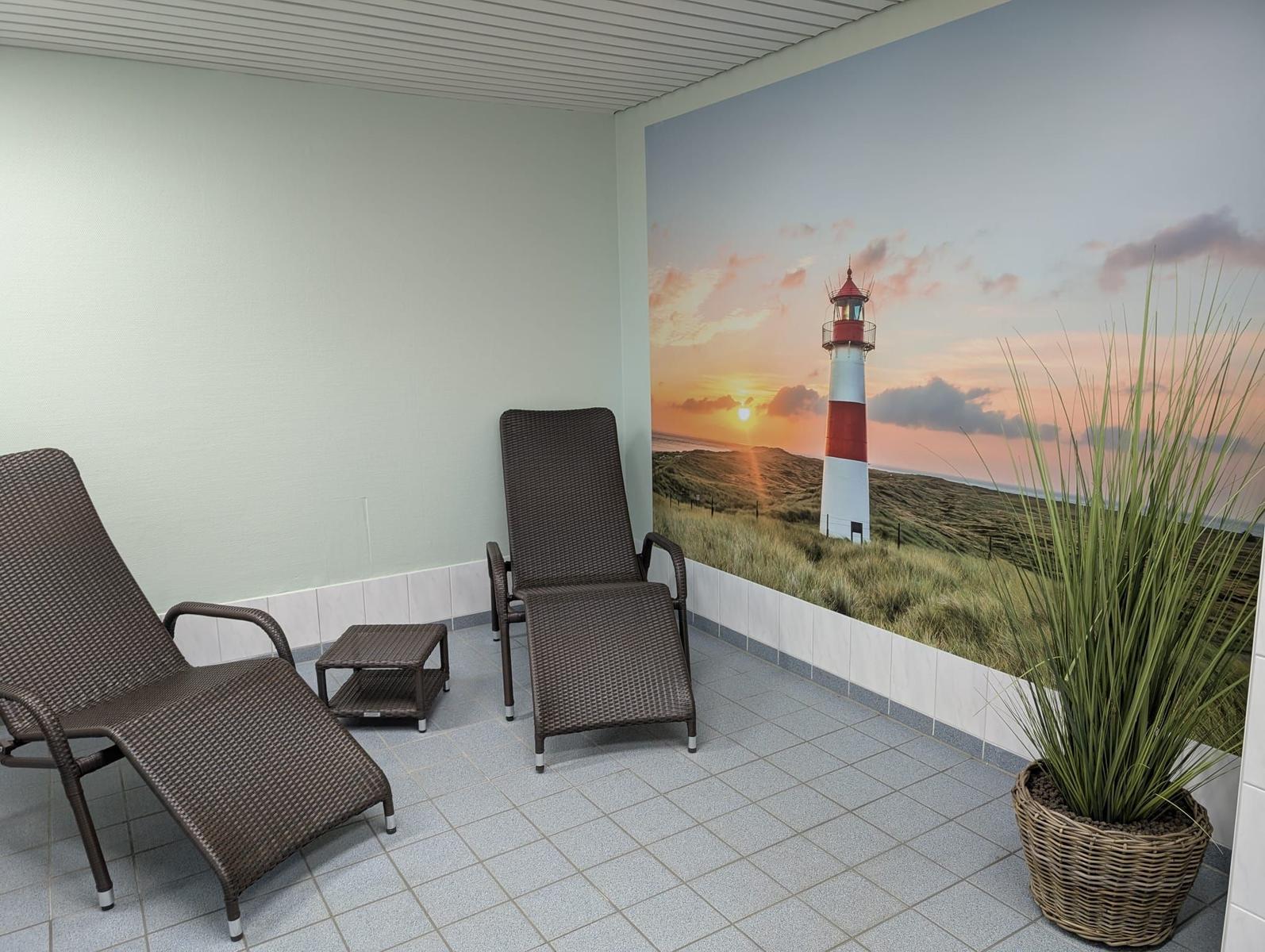 Terrasse mit zwei Liegestühlen und Pflanze. Wandbild zeigt Leuchtturm bei Sonnenuntergang.