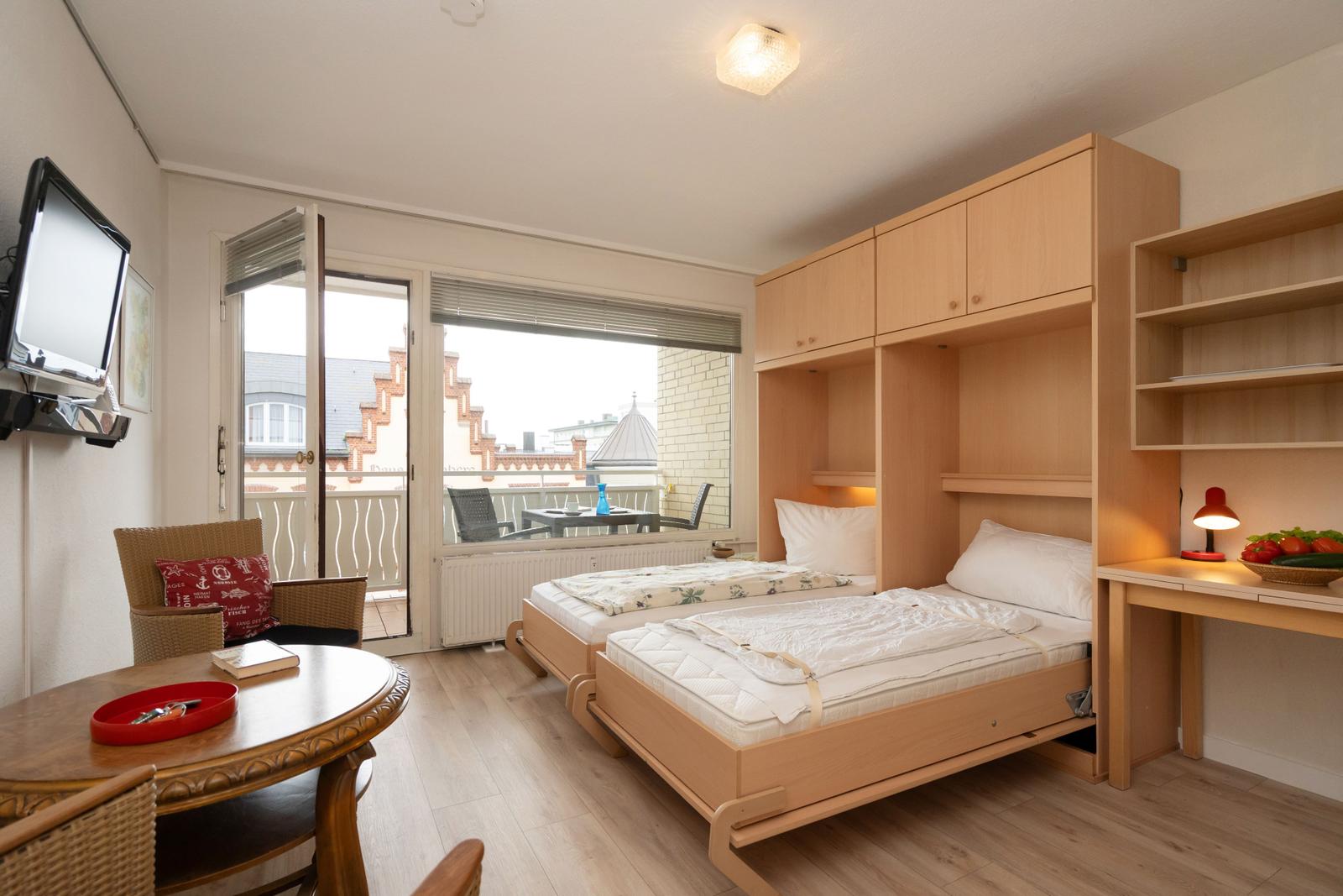 Zimmer mit zwei Betten, Schreibtisch und Balkon. Holzmöbel und Fernseher.