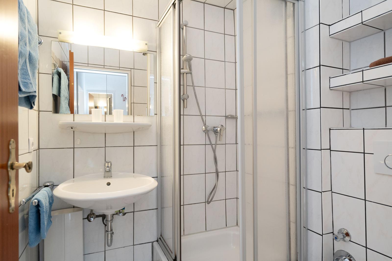 Badezimmer mit Dusche, Waschbecken und Spiegel.