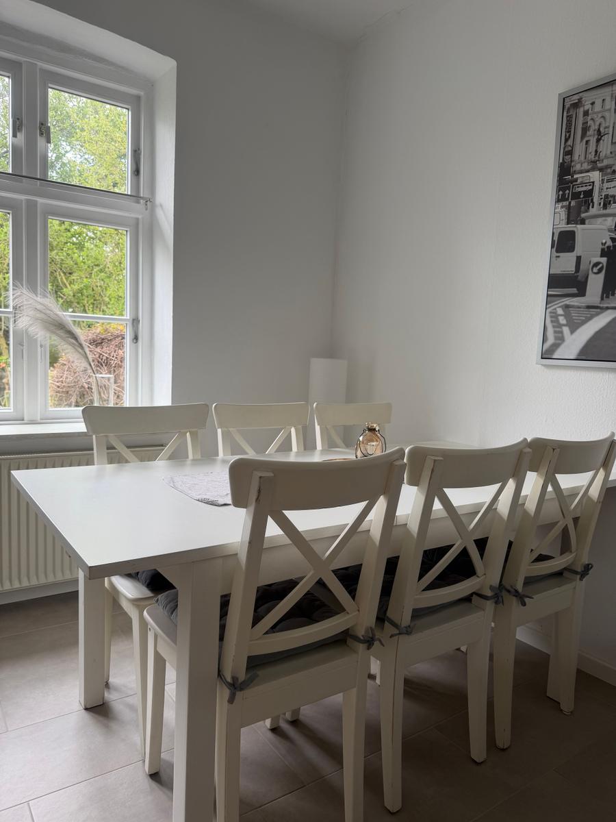 Esszimmer mit weißem Tisch und Stühlen, Fenster mit Blick auf Grün.