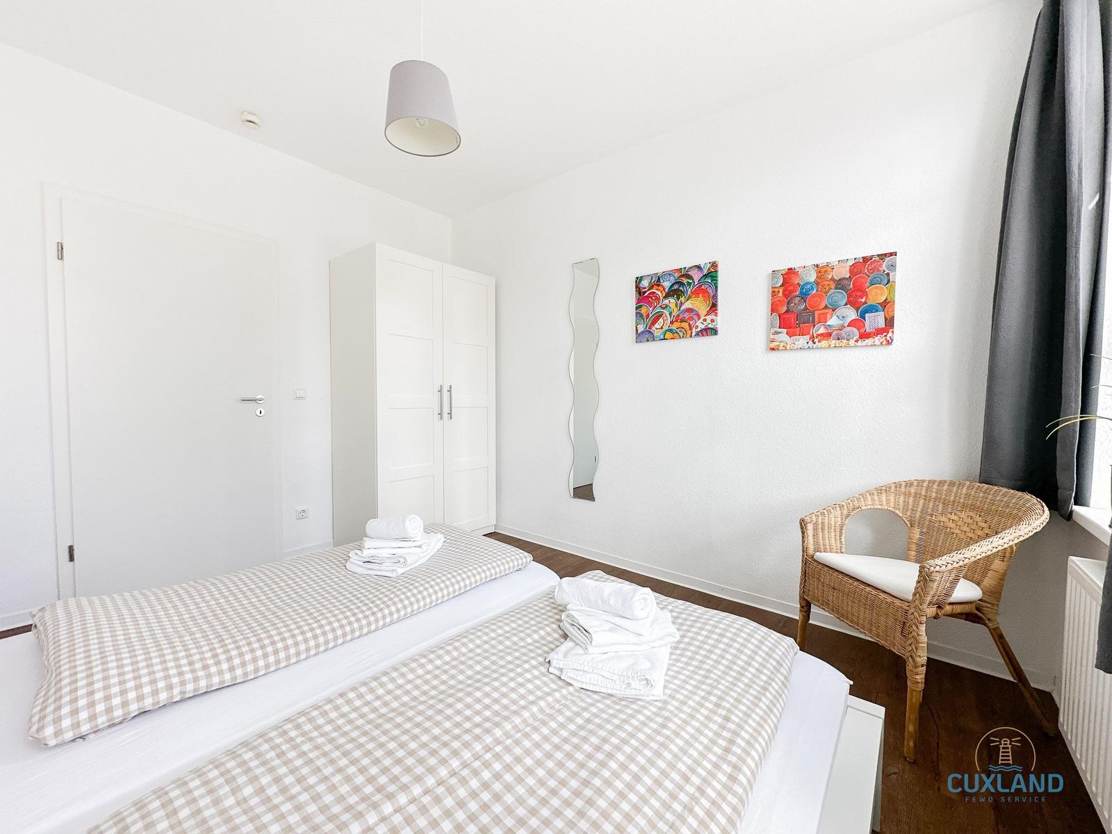 Schlafzimmer mit Doppelbett, Kleiderschrank, Sessel und Wandbildern.
