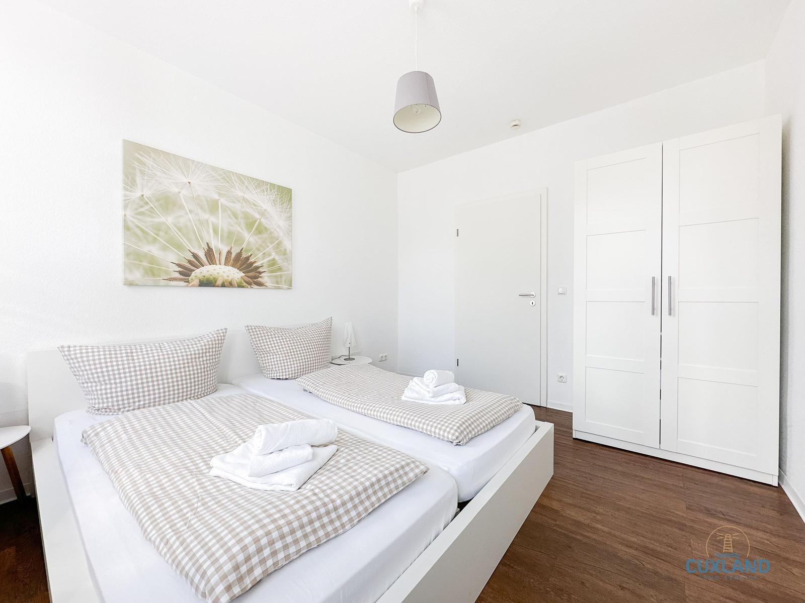 Zimmer mit zwei Betten, Kleiderschrank und Wandbild mit Löwenzahn.