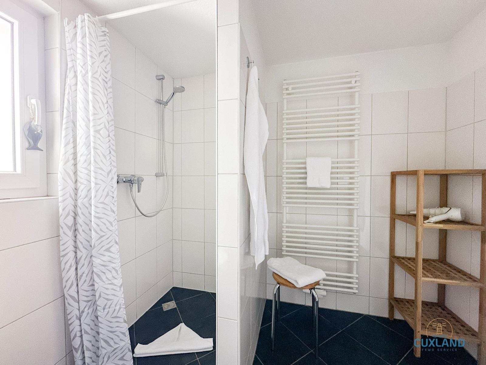 Badezimmer mit Dusche, Heizkörper und Holzregal.