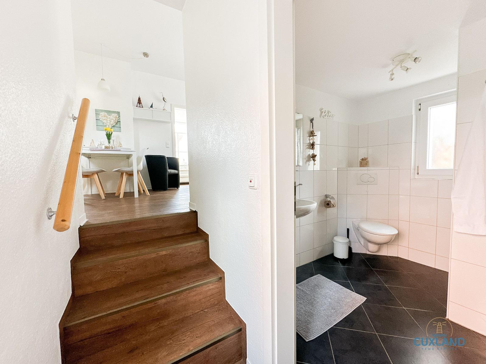 Treppenhaus mit Blick in Wohnbereich und Badezimmer mit Toilette und Waschbecken.