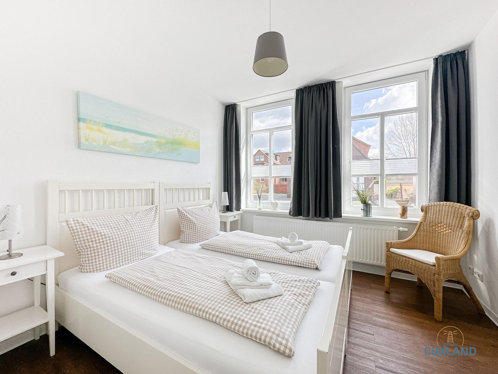 Zimmer mit Doppelbett, Fenster, Stuhl und Wandbild.