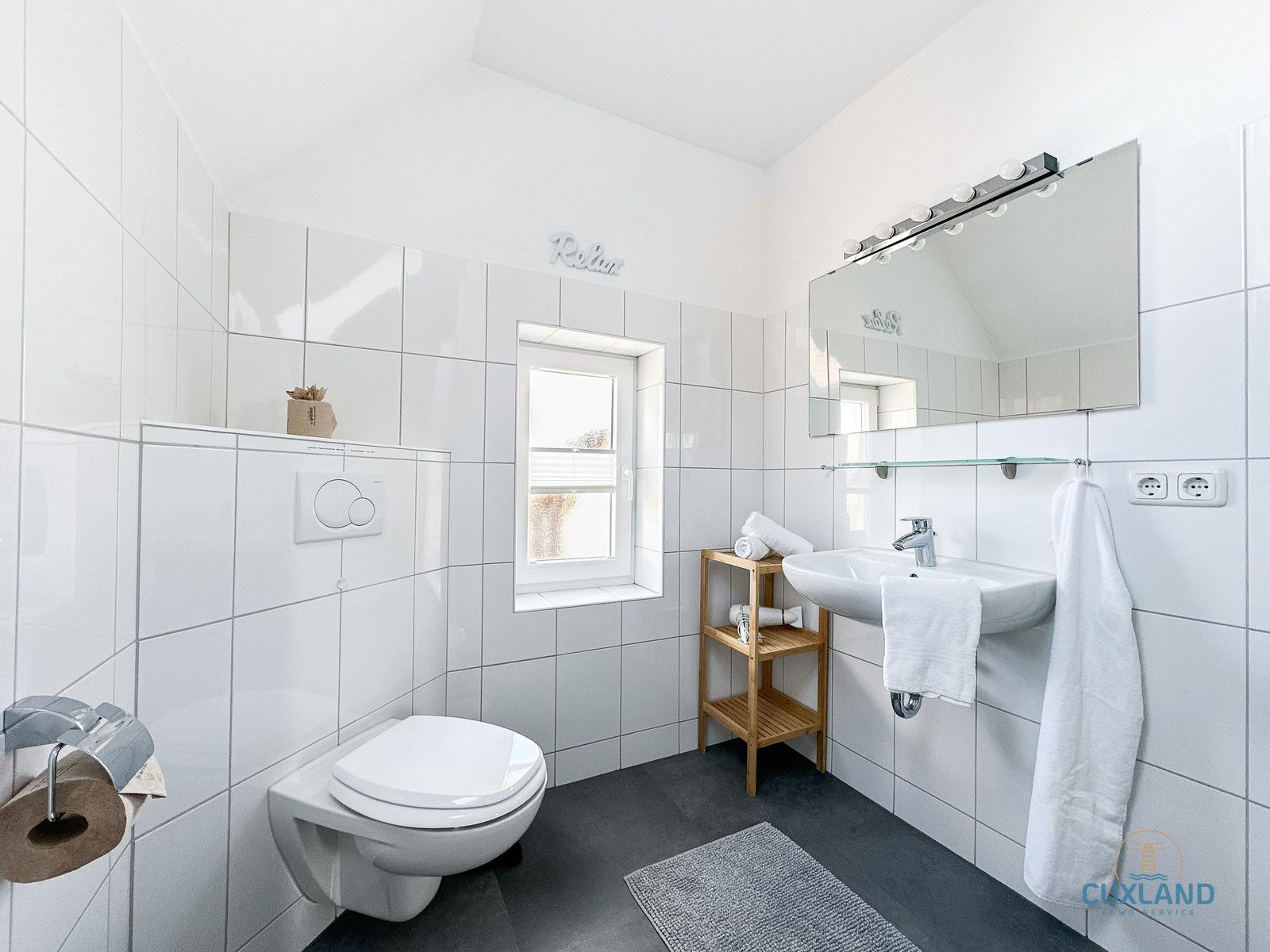 Badezimmer mit Toilette, Waschbecken und Dusche. Weiße Fliesen und dunkler Boden.