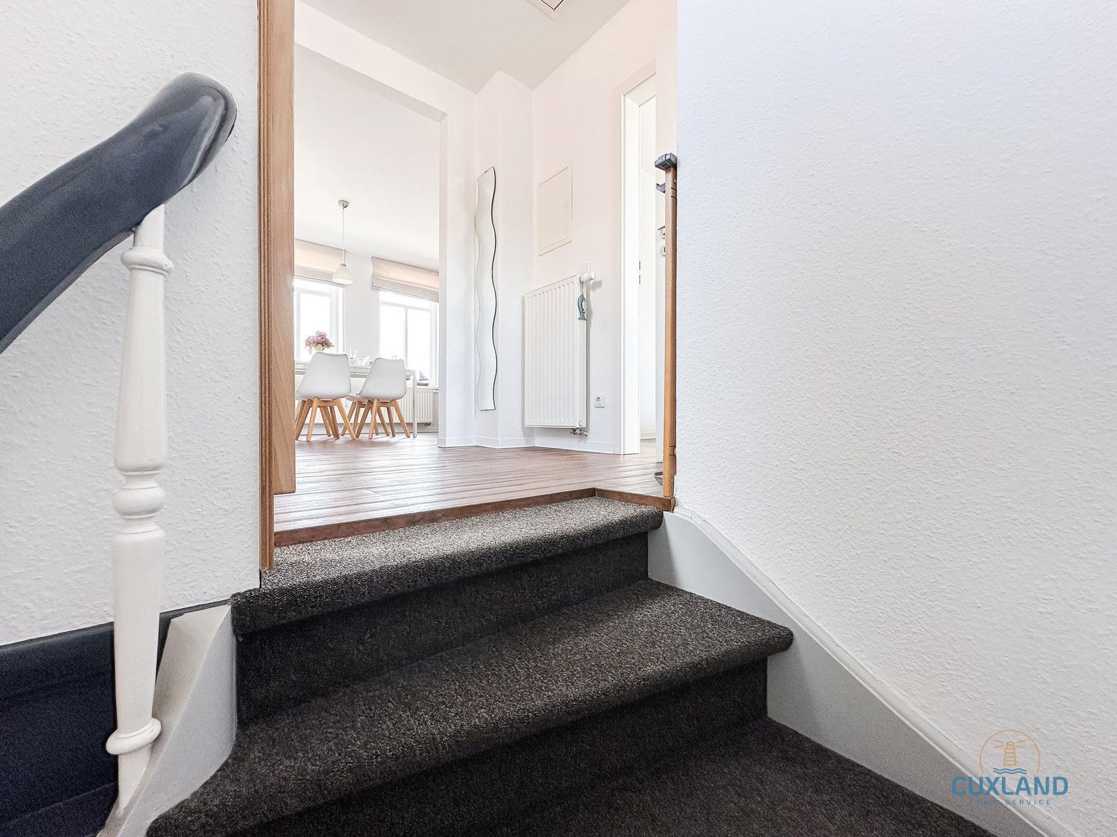 Treppe mit Teppichstufen führt in ein Wohnzimmer mit Esstisch und Stühlen.