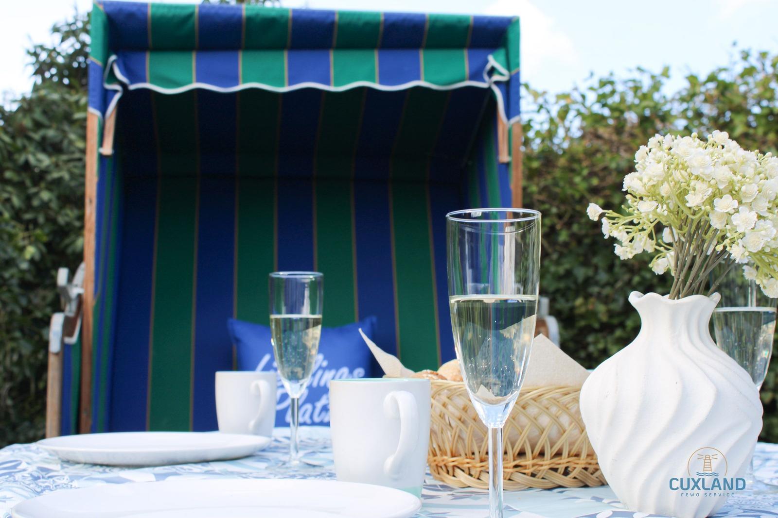 Tisch mit Gläsern, Tassen und Blumen vor Strandkorb