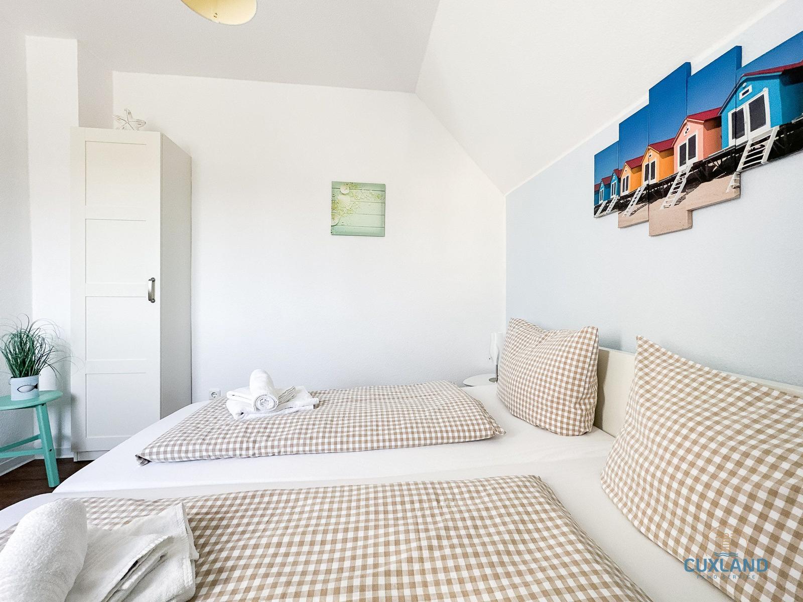 Schlafzimmer mit Doppelbett, Kleiderschrank und Wandbild von Strandhütten.