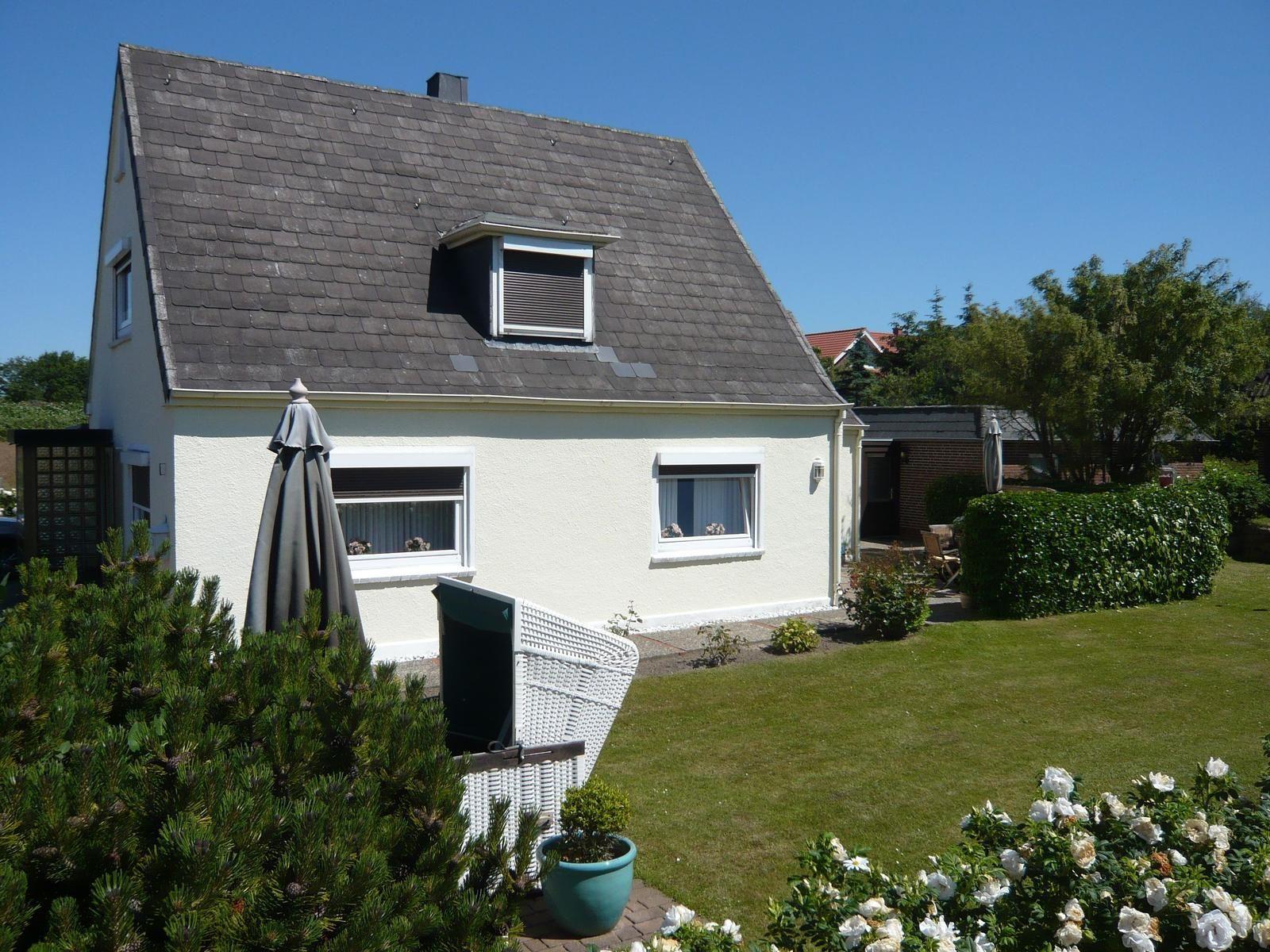 House with garden, parasol, and flower beds. Skylight and white facade.