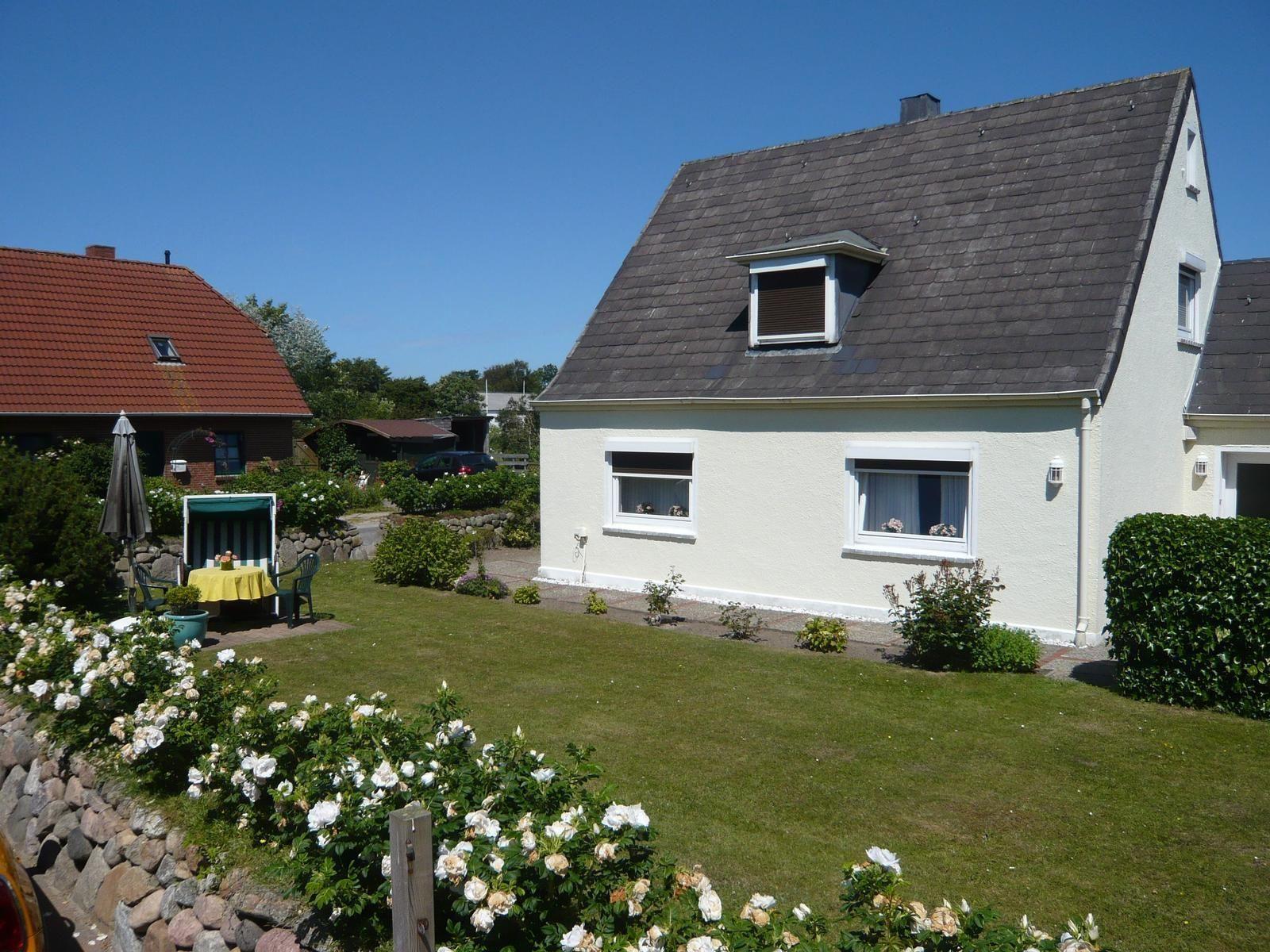House with garden, flower beds, and terrace under blue sky.