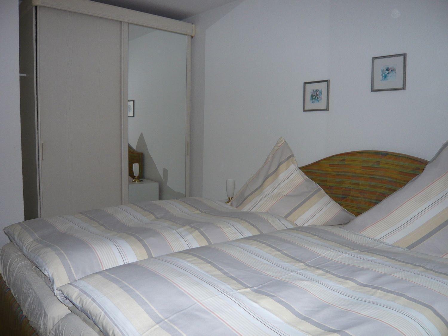 Two beds with striped bedding, sliding wardrobe, and two pictures on the wall.