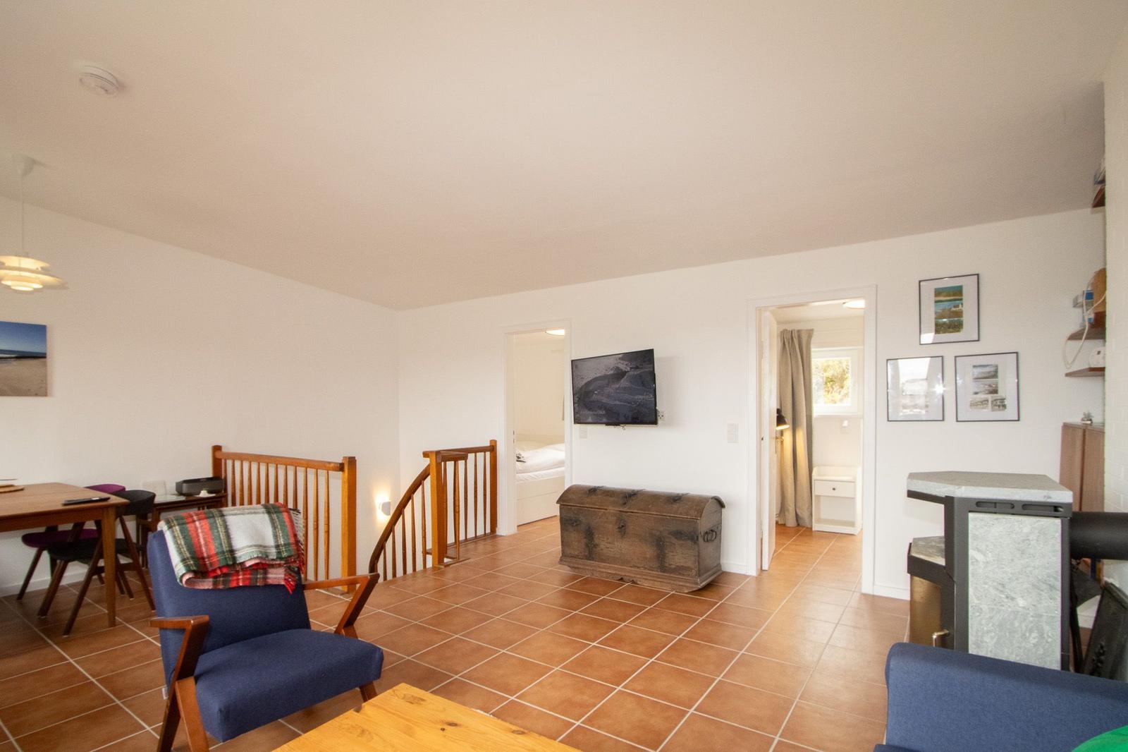 Living area with wooden staircase, TV, and wood-burning stoves. Kitchen and bedroom are visible.