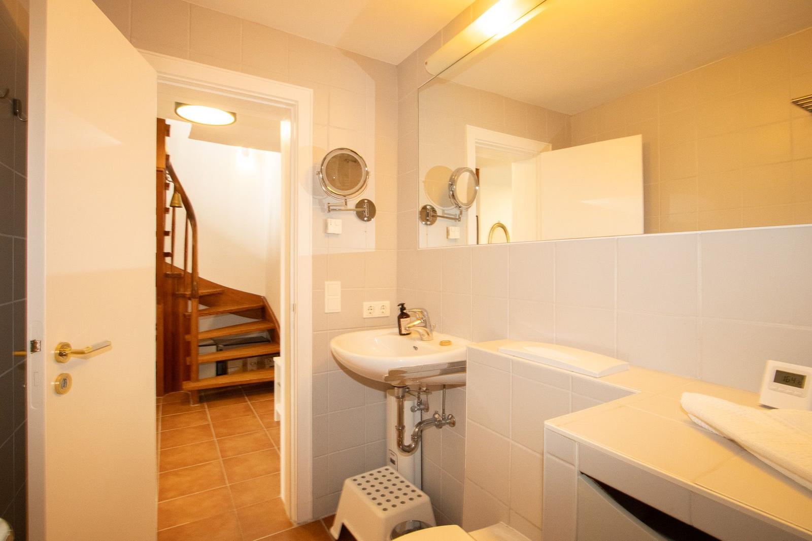 Bathroom with sink, mirror, and staircase in the background.