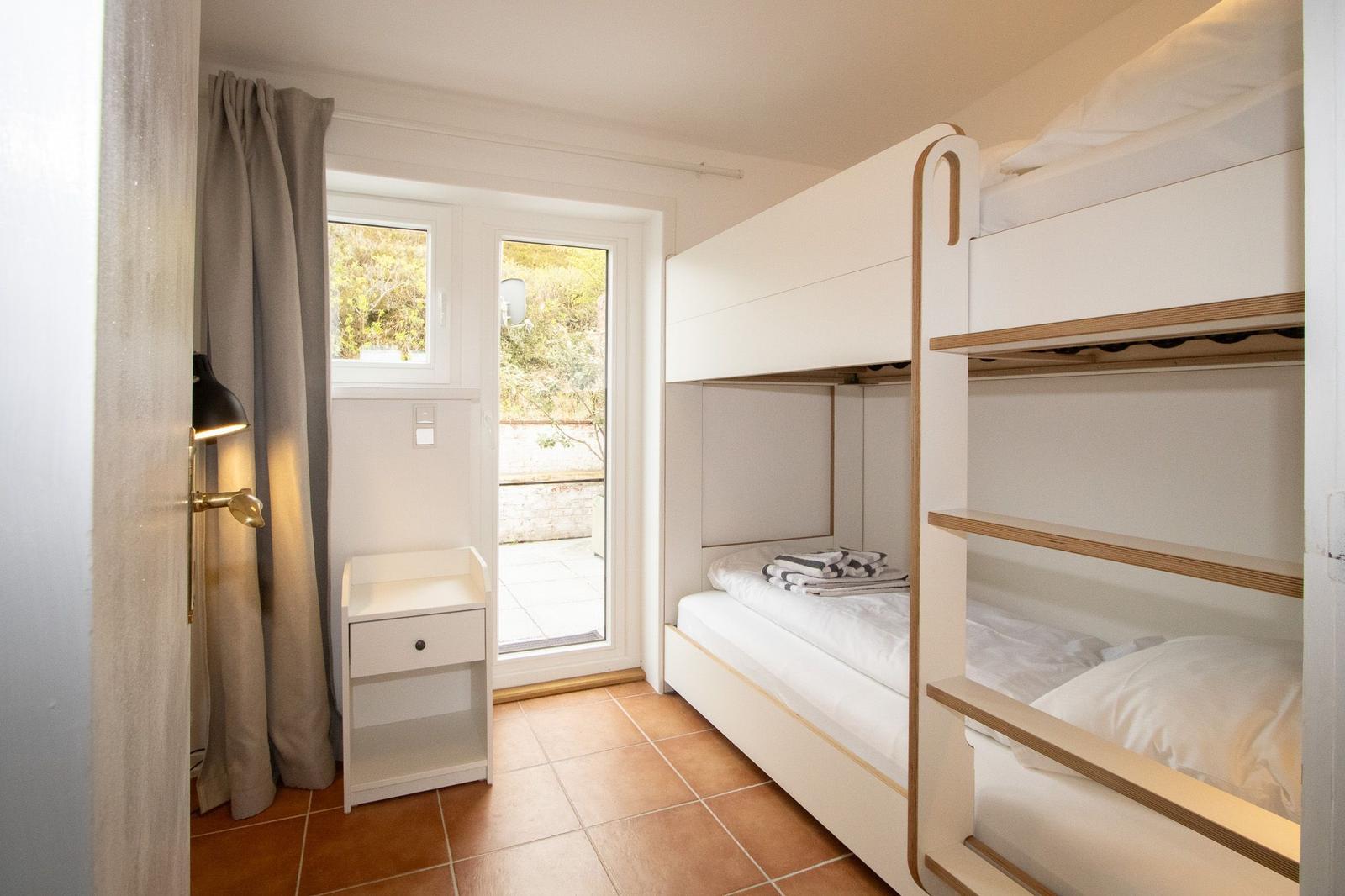 Room with bunk bed, window, and small cabinet.