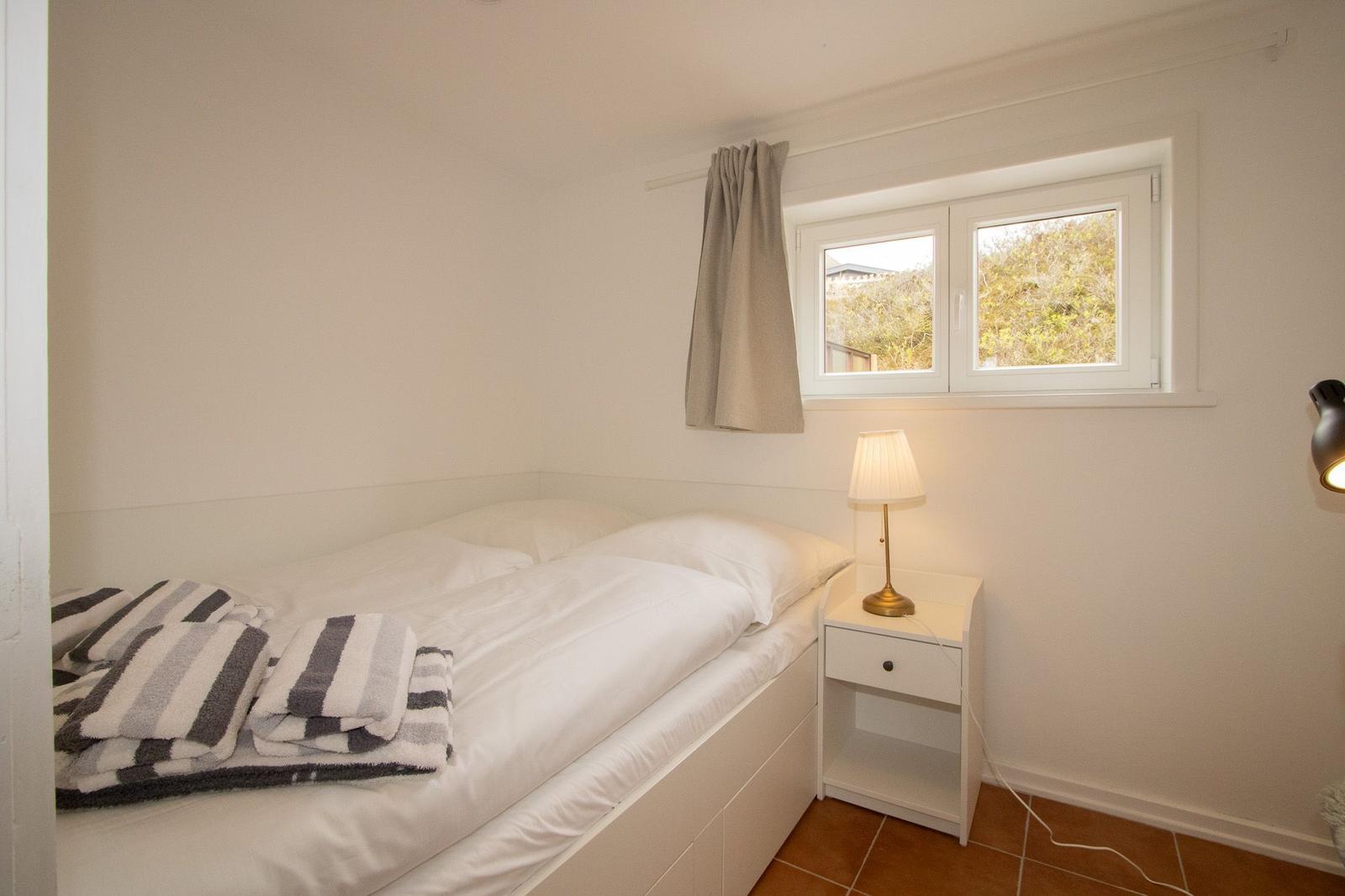 A bedroom with a bed, nightstand, and window. Folded towels are on the bed.