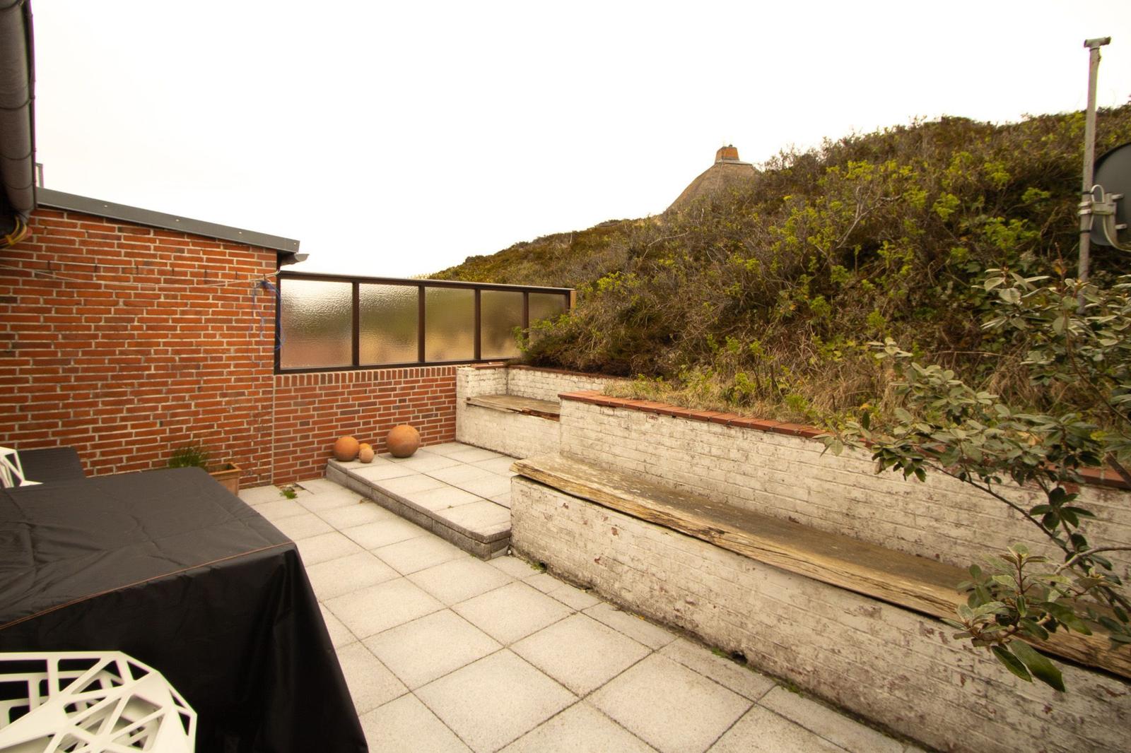 Terrace with table, benches, and view of green hills.