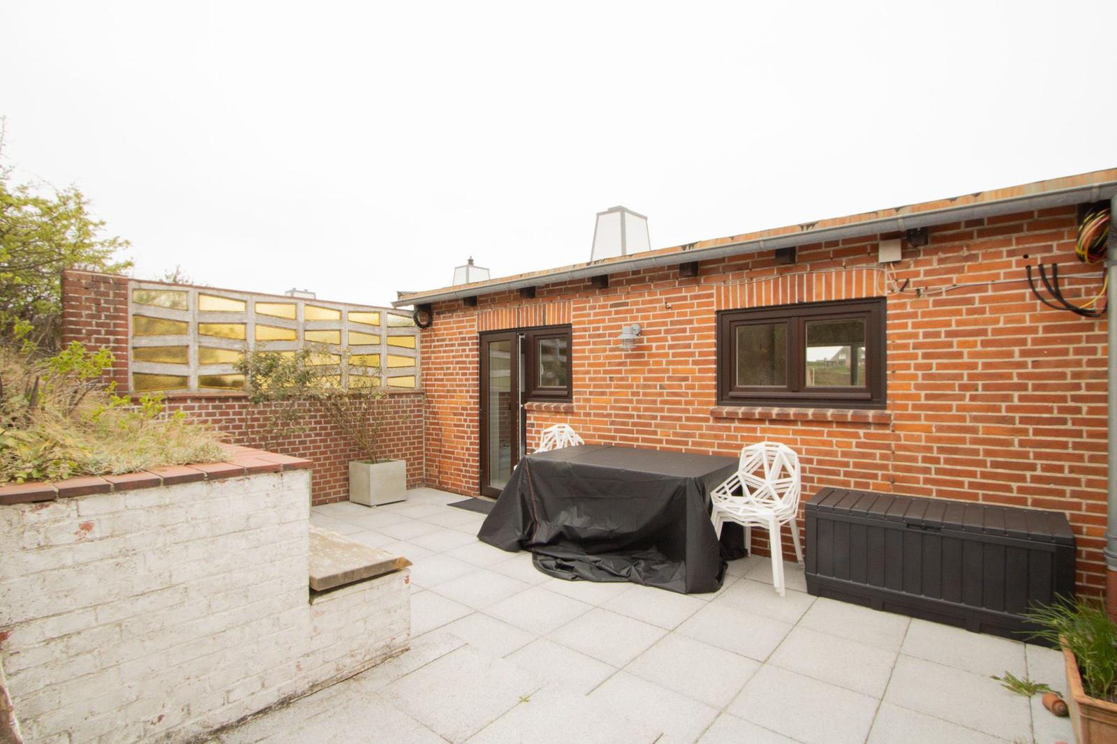 Terrace with table, chairs, and garden furniture beside red brick house