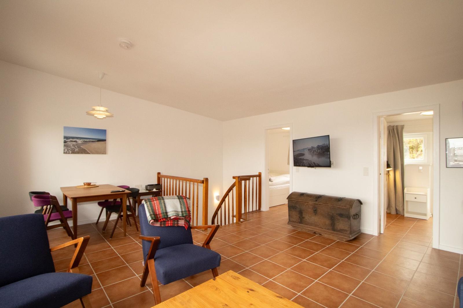 Living area with dining table, seating, and TV. Staircase to bedroom.