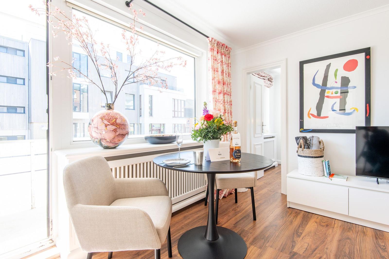 Dining area with table, chairs, and window view. Wall art and TV are visible.