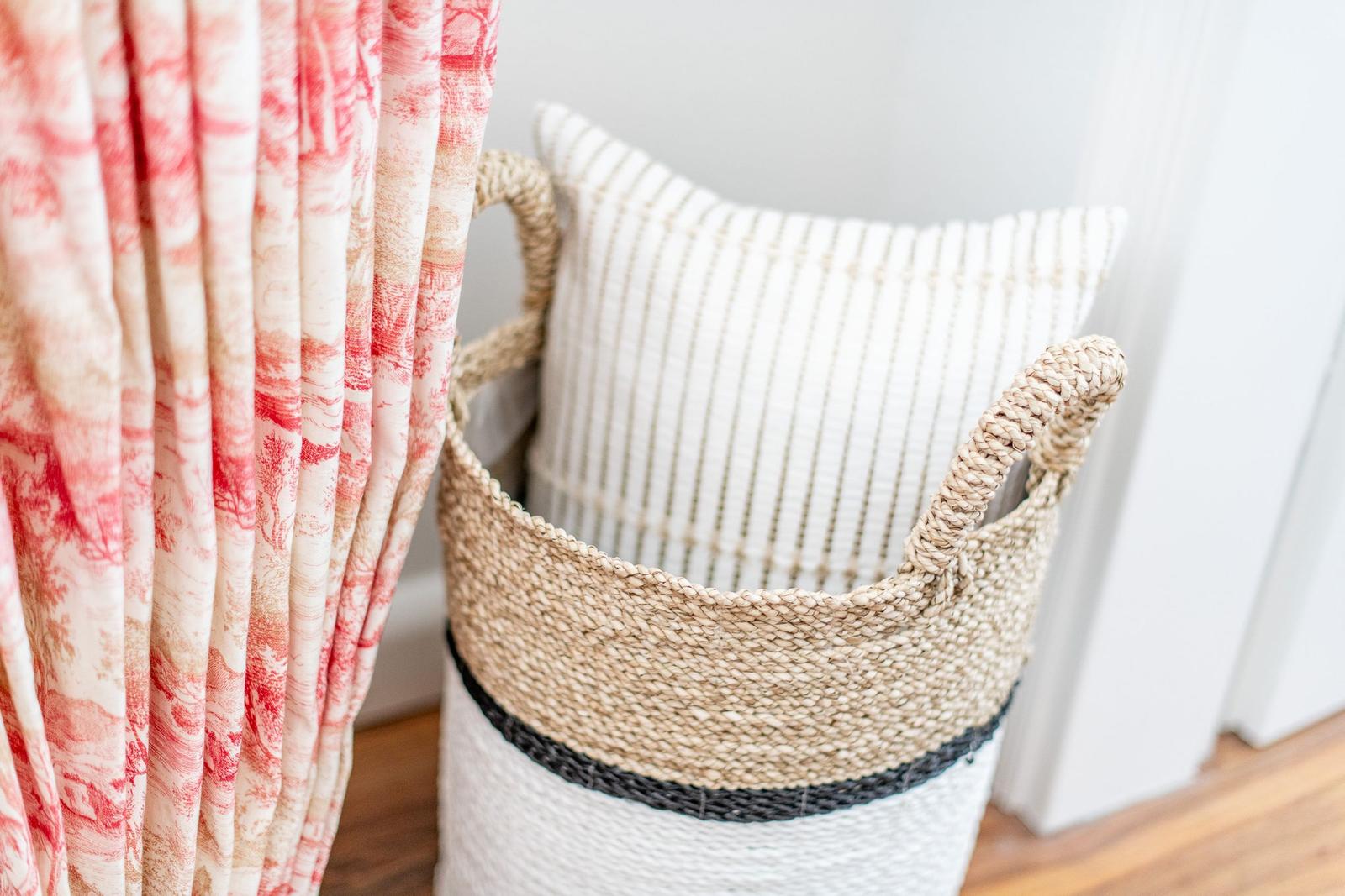 A basket with a pillow is next to a curtain.