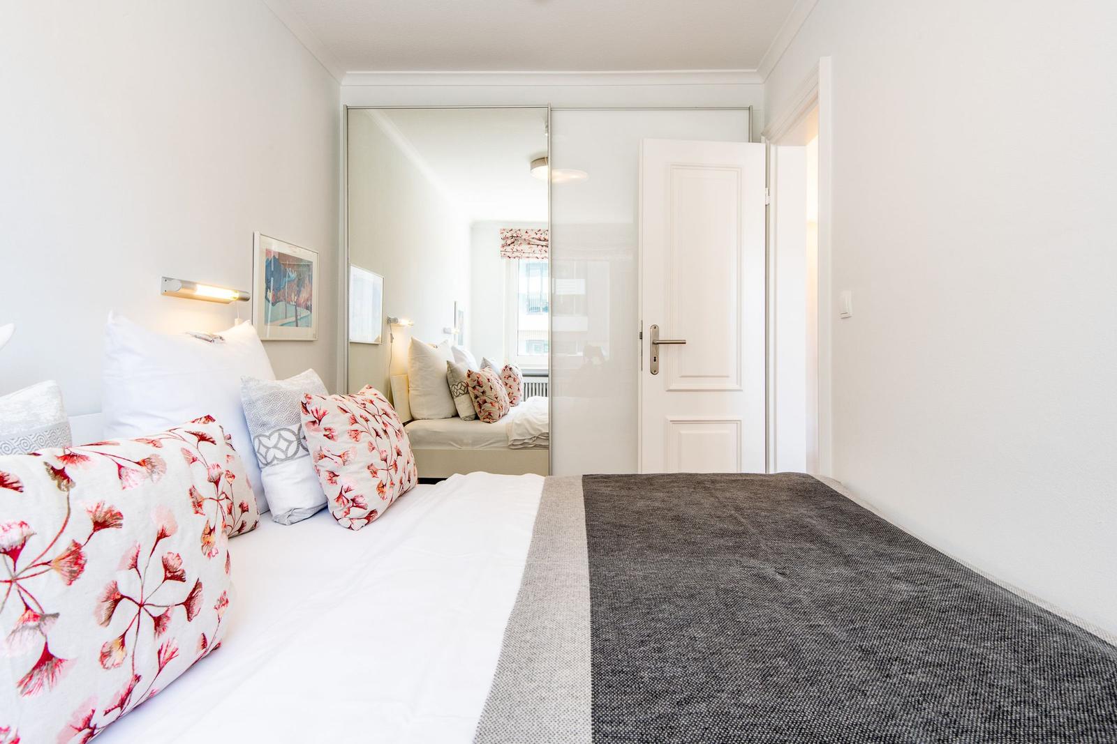 Bedroom with bed, pillows, and mirrored closet. Door leads to a hallway.