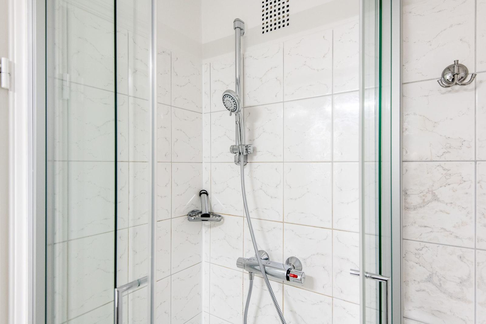 Shower with glass enclosure and chrome fixtures on white marble tiles