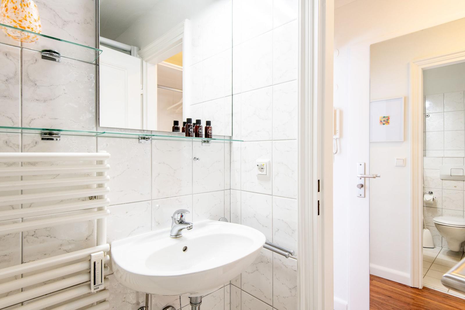 Bathroom with sink, mirror, and heater. Toilet area is adjacent.