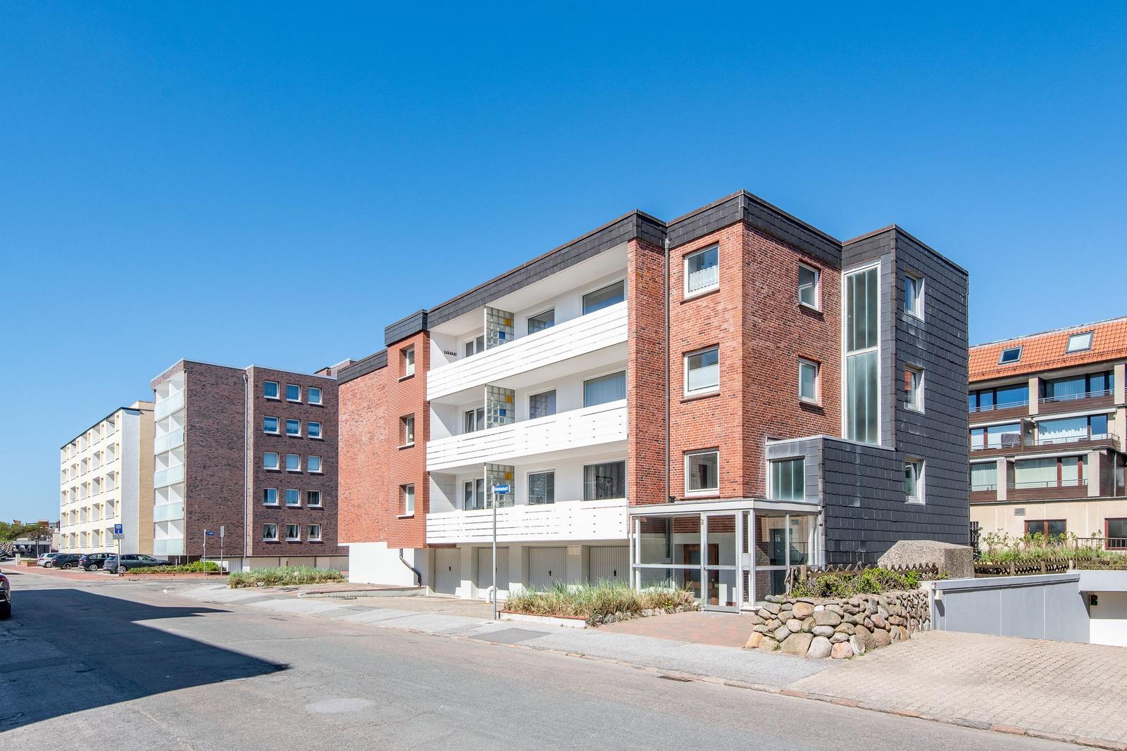 Modern multi-family house with balconies and glass facade. Street with parked cars.