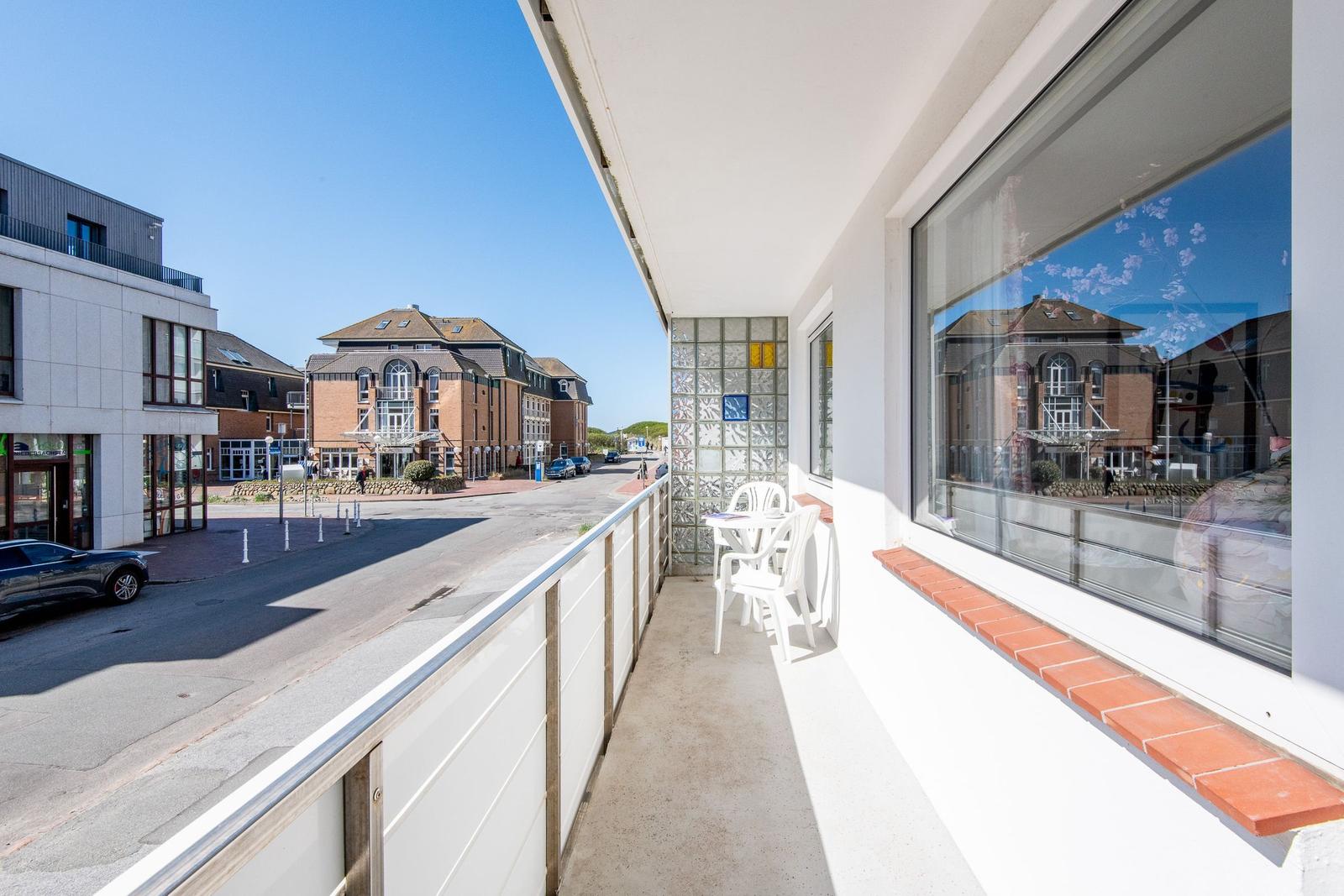 Balcony with white chairs and table. View of street and buildings.