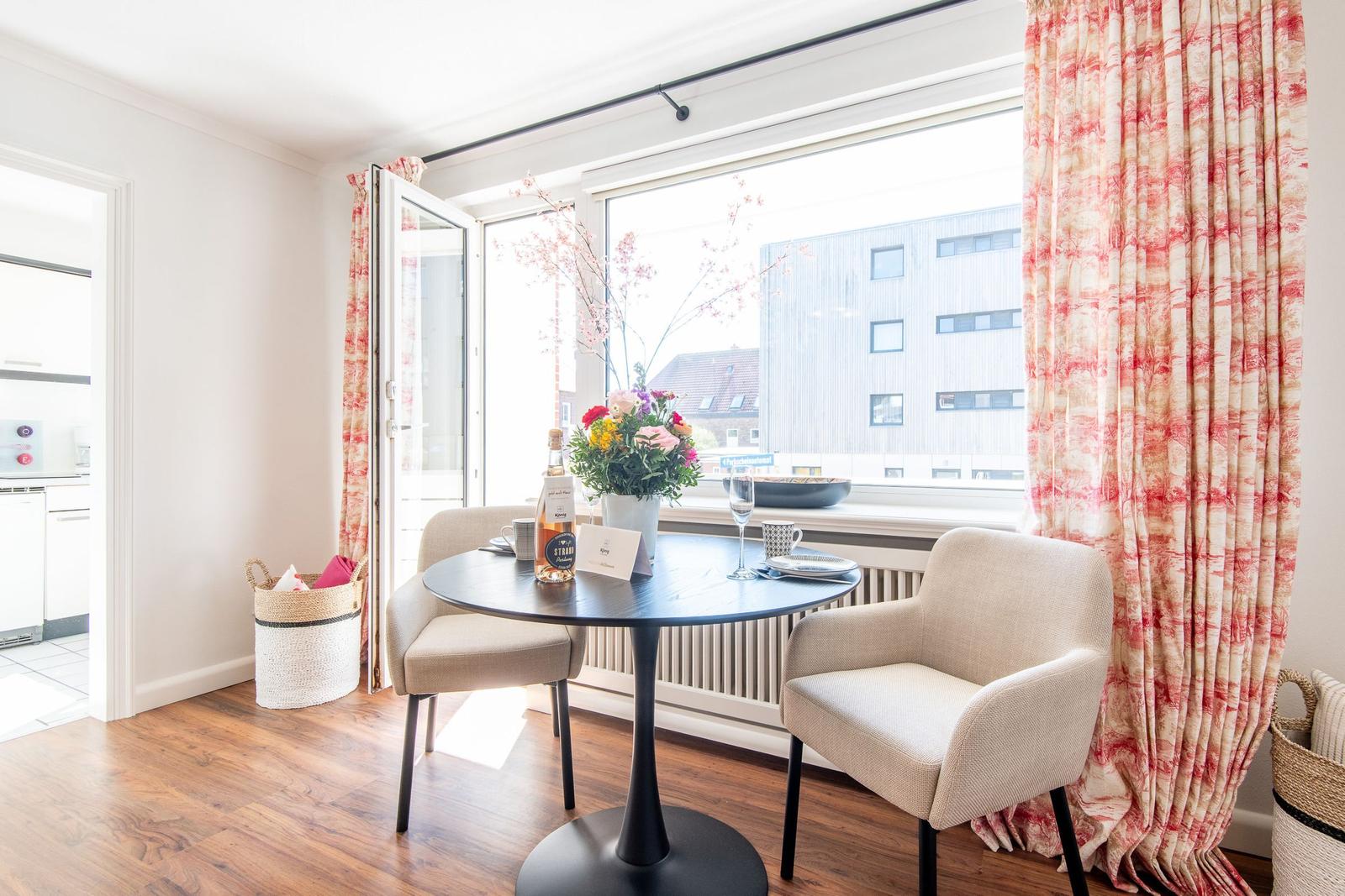 Dining table with two chairs in front of large window overlooking buildings.