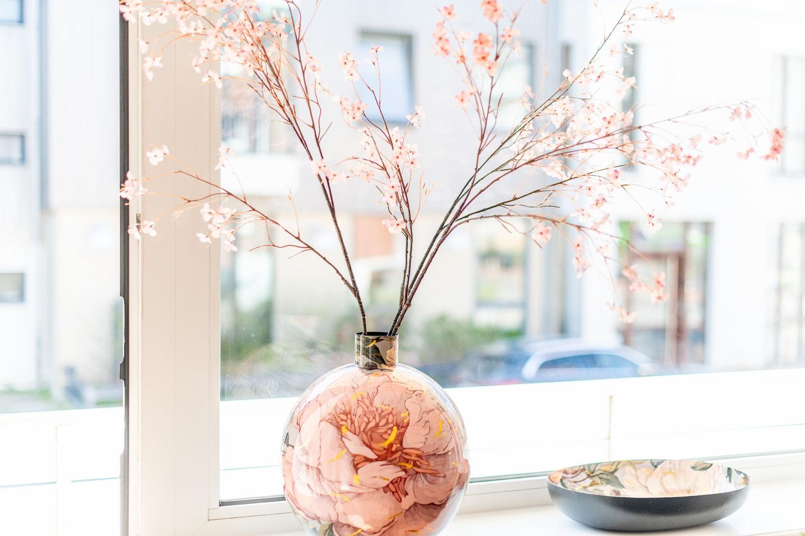 On the windowsill, there is a vase with cherry branches and a bowl.