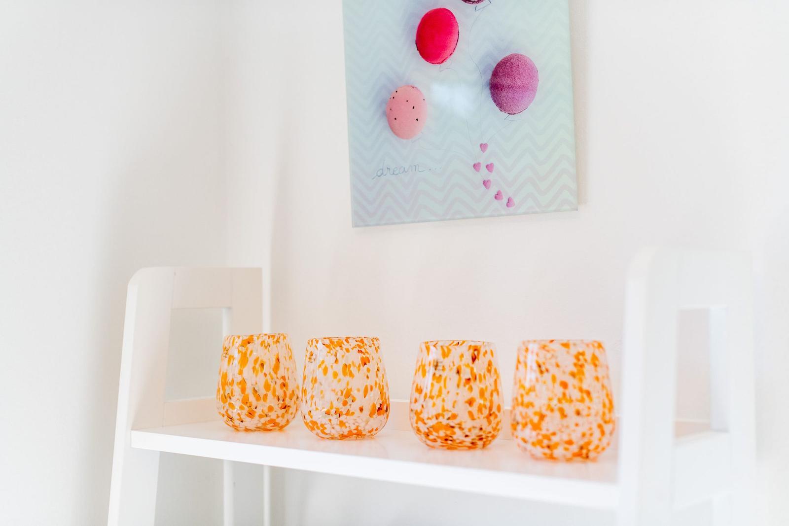 Four orange-speckled glasses sit on a white shelf.