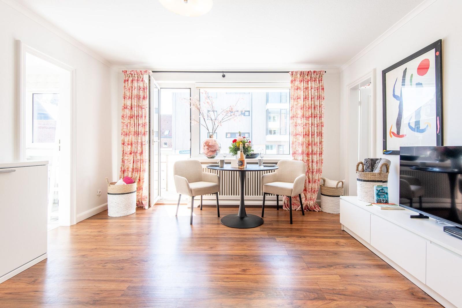 Living room with dining table, two chairs, TV, and windows with curtains.