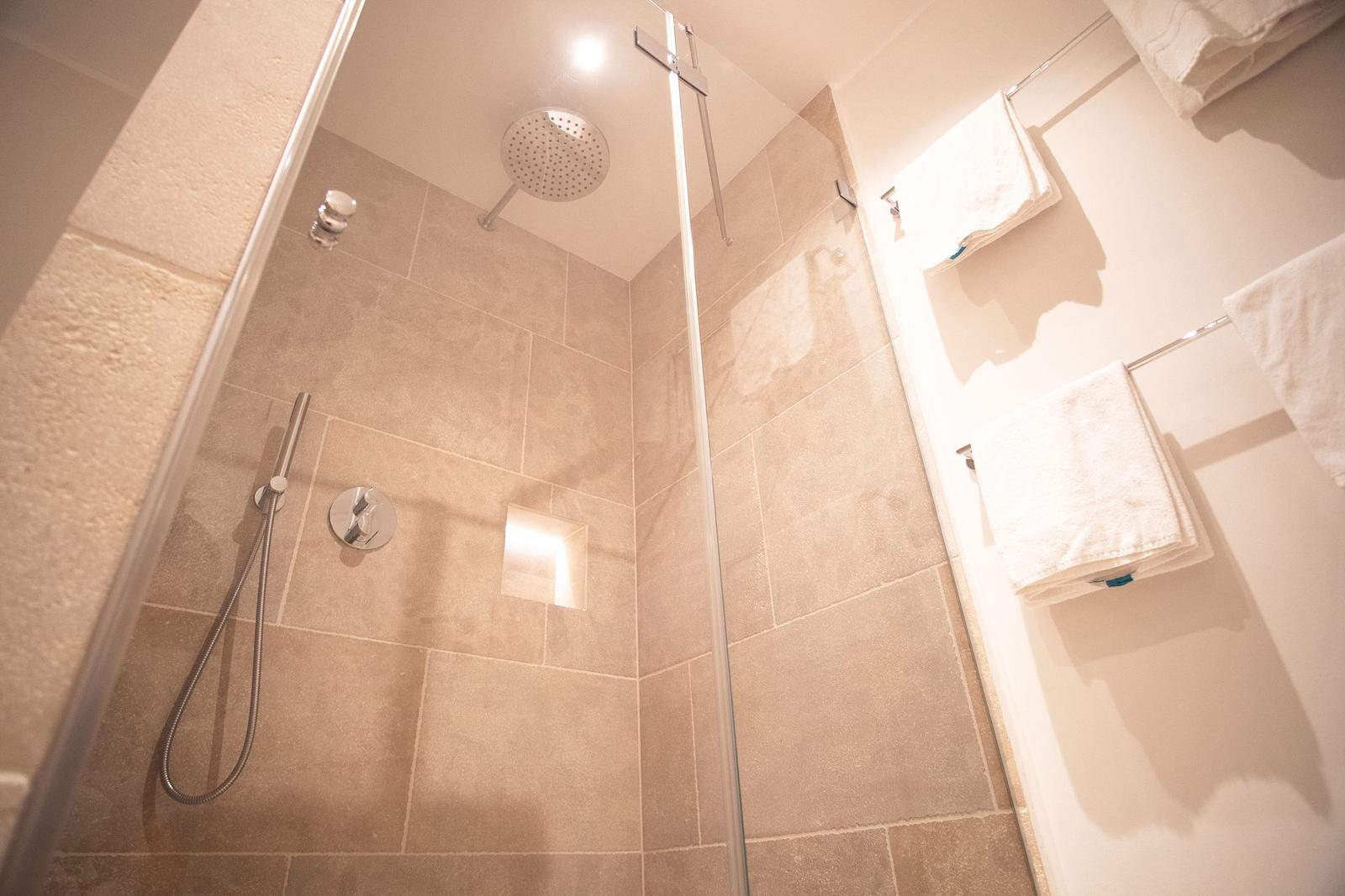 Dusche mit Duschbrause und Handbrause, Wandfliesen und Handtücher.
