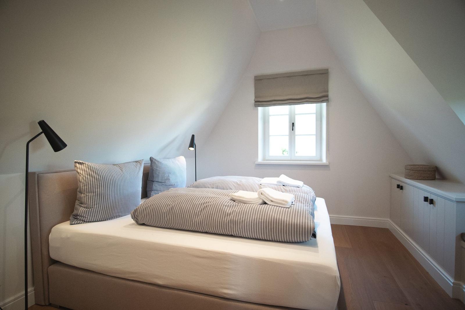 Schlafzimmer mit Dachschräge, Bett, Fenster und Nachttisch.