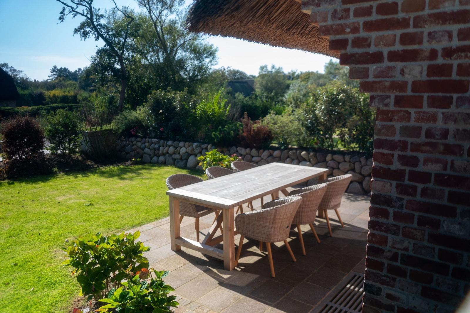 Terrasse mit Tisch und Stühlen, umgeben von Garten und Steinmauer.