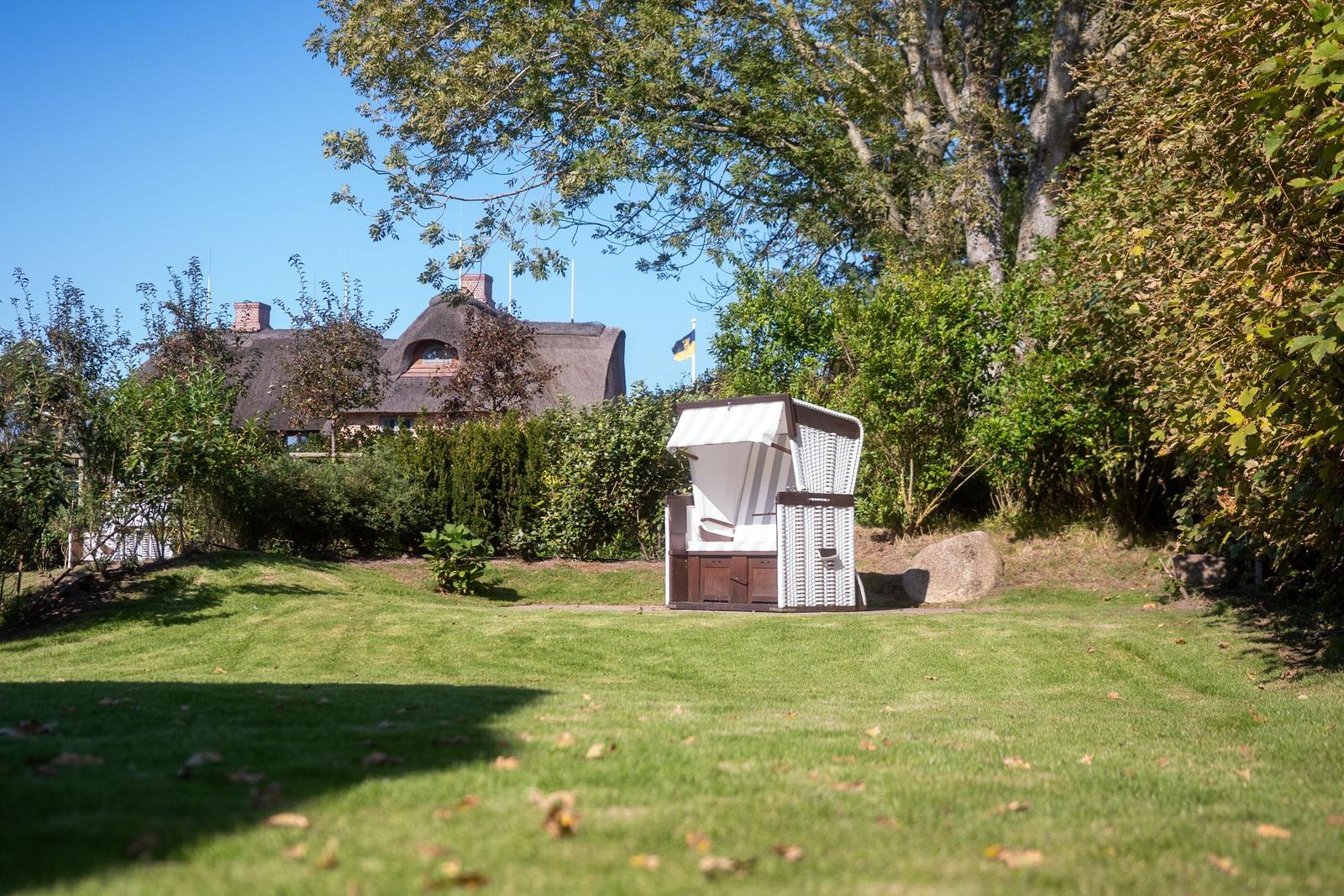 Haus mit Strohdach, Garten mit Liegestuhl und Bäumen.