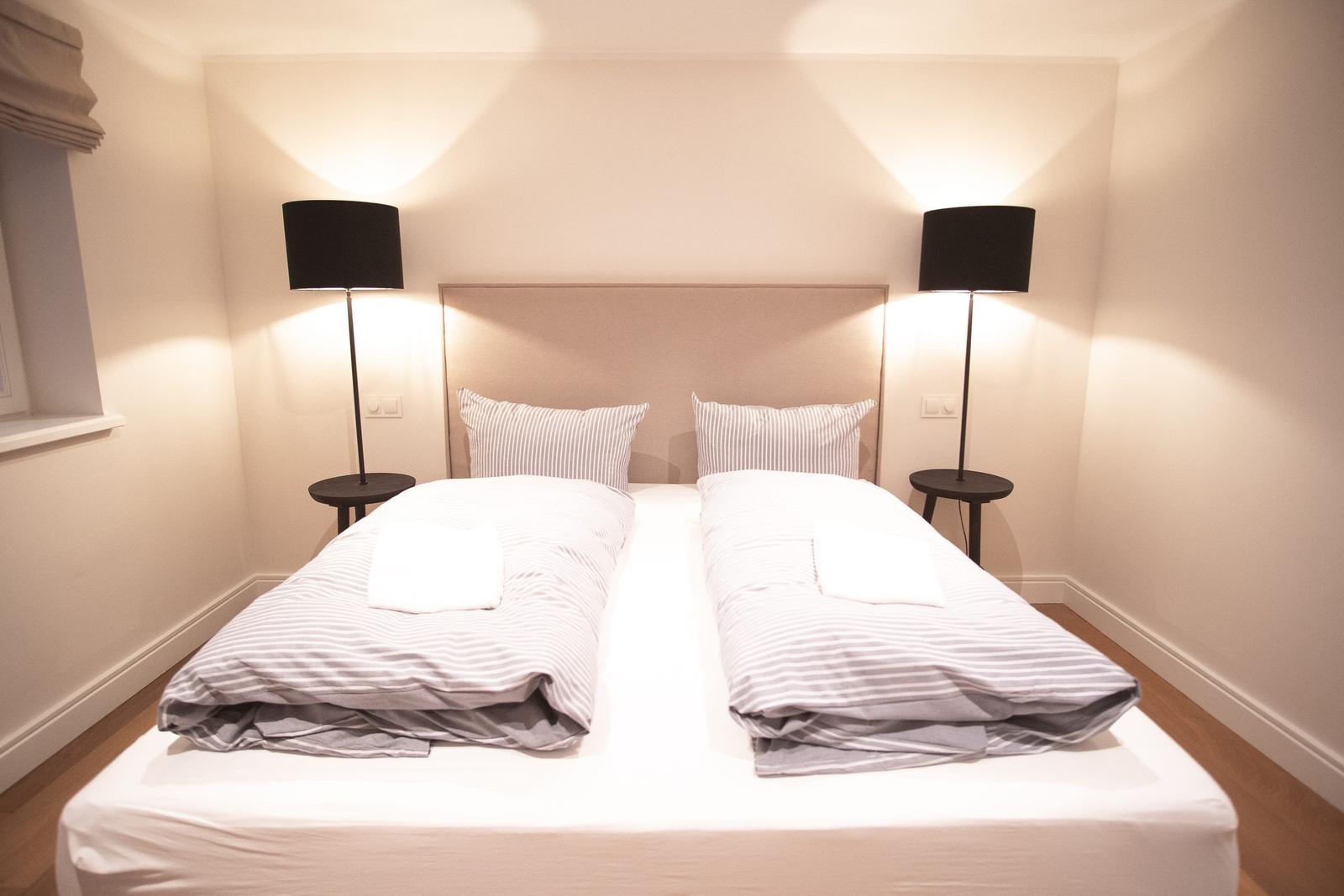 Doppelbett mit zwei Kissen und zwei Nachttischen mit Lampen.