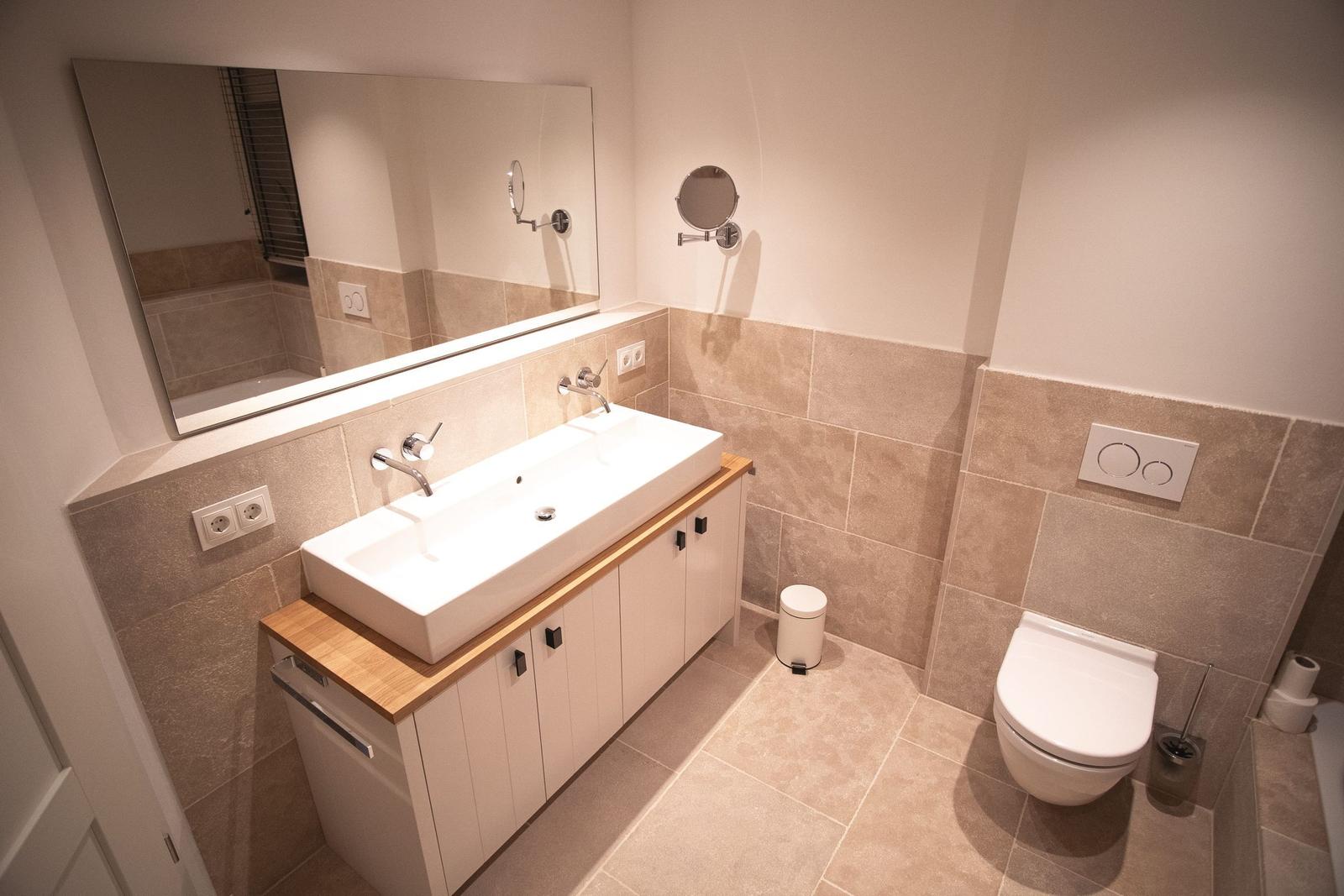 Badezimmer mit Waschbecken, Spiegel und Toilette. Fliesenwand und Boden.