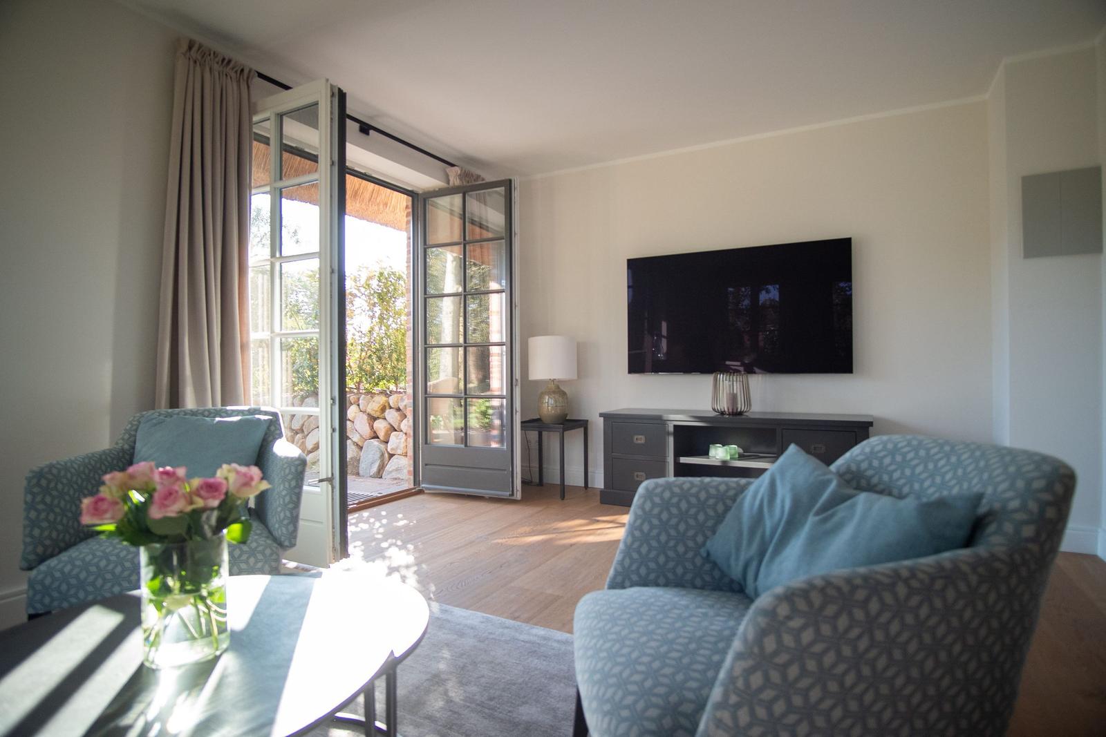 Wohnzimmer mit zwei Sesseln, Fernseher und Terrassentür.