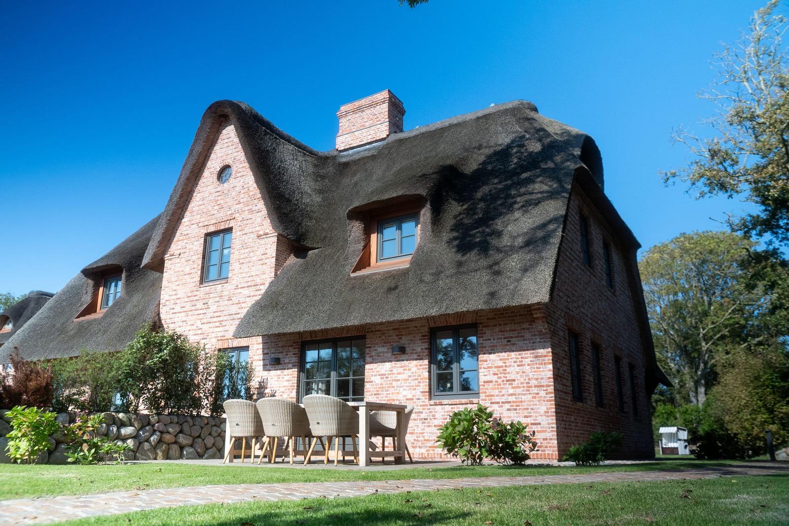Haus mit Strohdach und Steinmauer, Außenbereich mit Sitzgruppe.