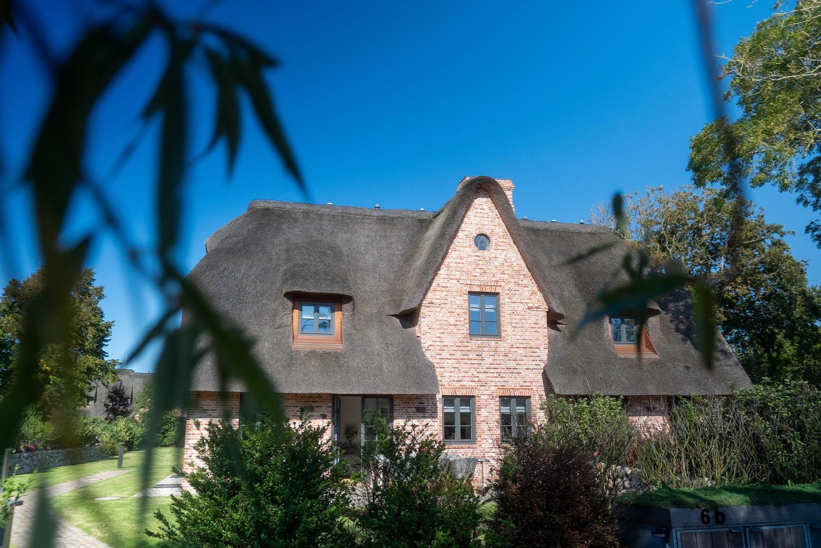 Haus mit strohgedecktem Dach und Backsteinfassade im Grünen.
