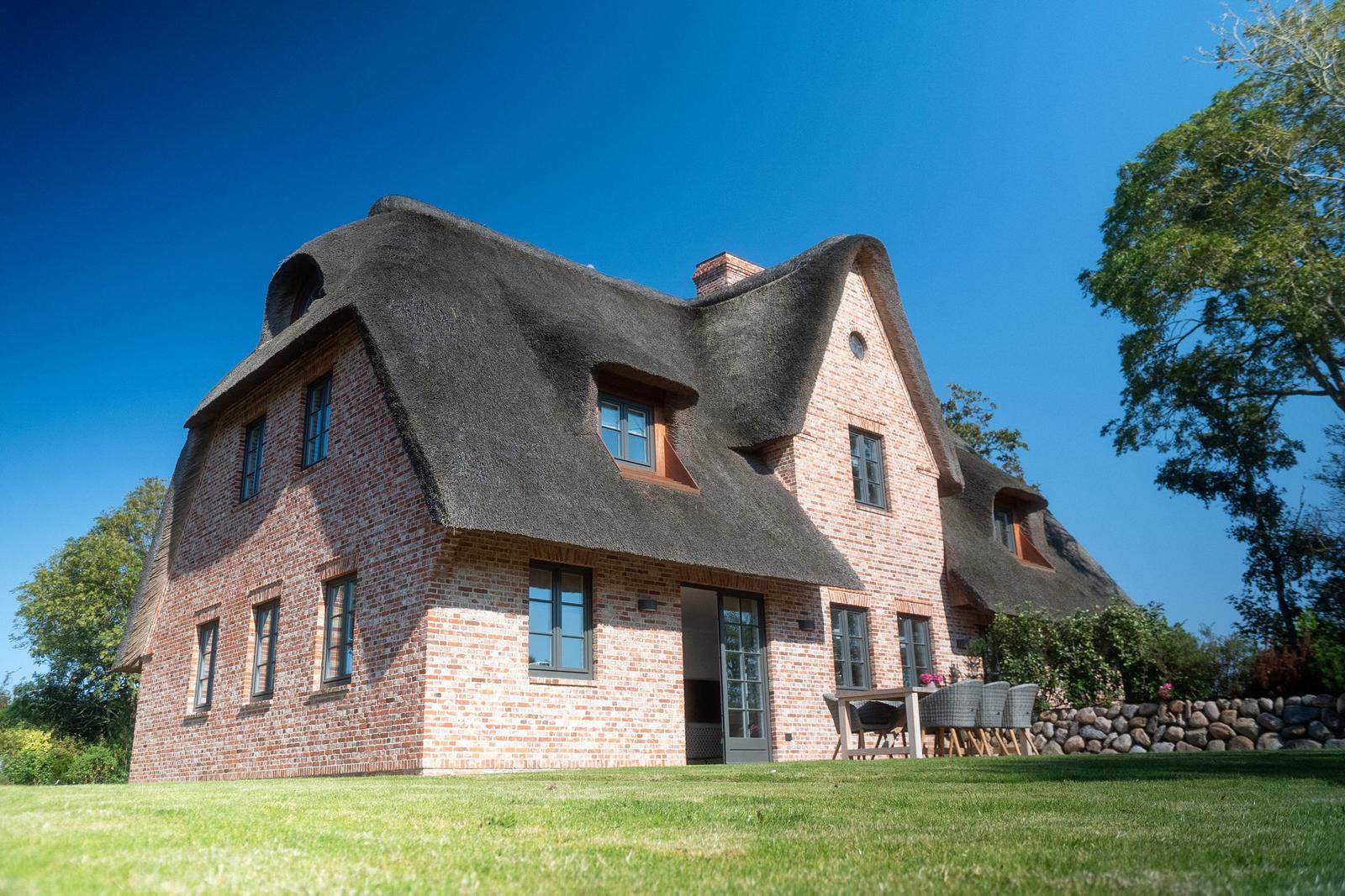 Rotes Backsteinhaus mit Strohdach und Terrasse im Grünen.