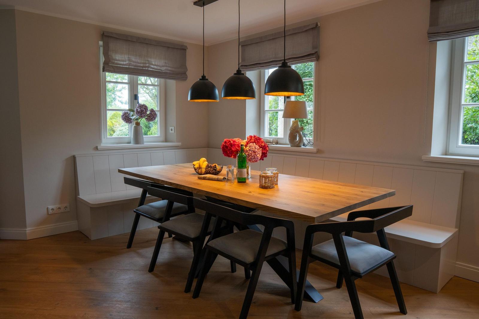 Esszimmer mit Holztisch, Sitzbänken und drei Hängelampen.