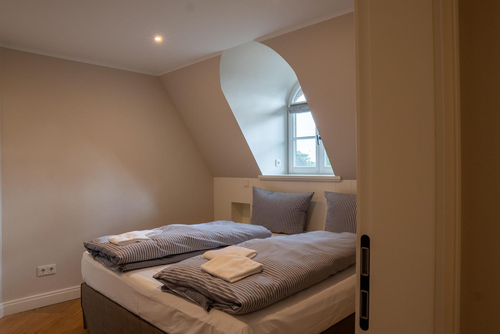 Schlafzimmer mit Doppelbett und schräger Wand. Fenster mit Bogenform.